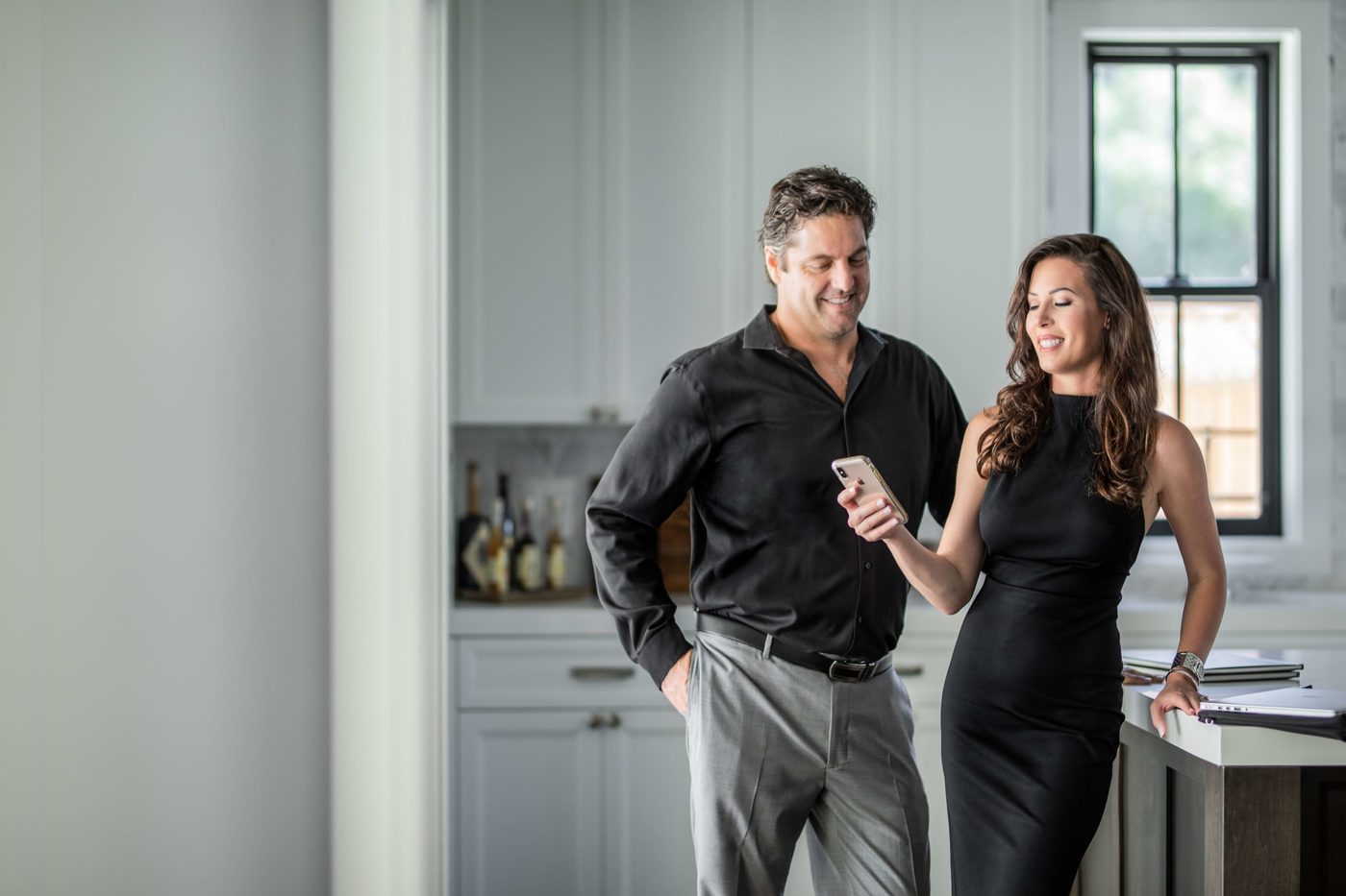 Couple in black outfits looking at phone in a bright kitchen