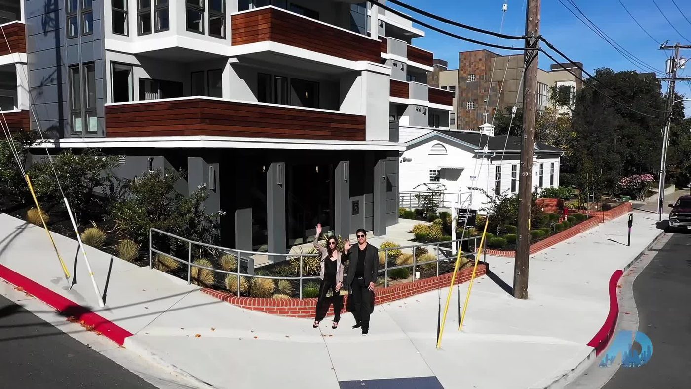Two people walking past modern apartment building on a sunny day
